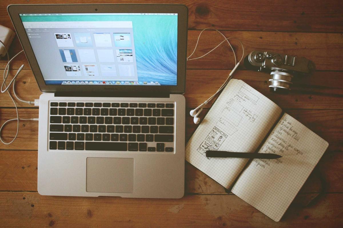 A laptop, a sketchbook and a camera on a wooden desk